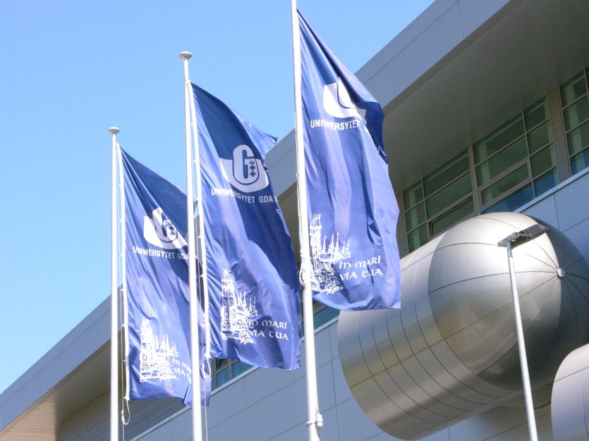 Flagi uczelni powiewające na tle budynku Biblioteki Głównej UG