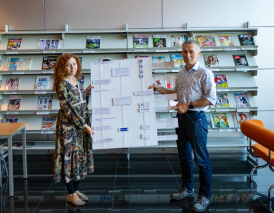 Mgr Agnieszka Wasilewska and mgr Zbigniew Ruszczyk holding one of the games created by the Section - a board that depicts the process of preparing a research data management plan.