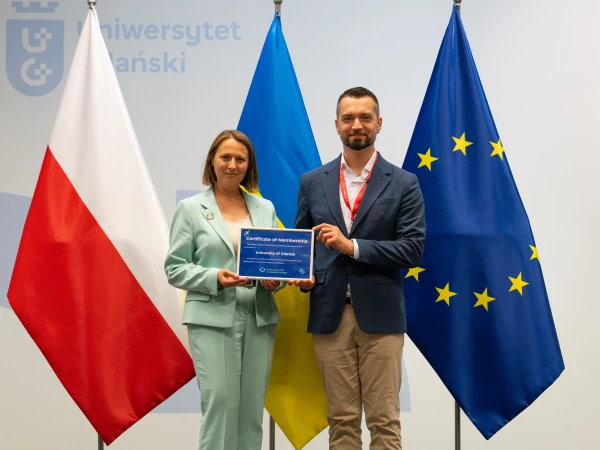 prof. Ewa Szymczak i Wołodymyr Szejko z cerytfikatem członkowstwa w GCUS; w tle flagi Polski, Ukrainy i UE