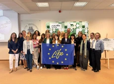 Zdjęcie grupowe uczestników seminarium; stoją na tle planszy z nazwą projektu, przed sobą trzymają flagę opartą na fladze UE z napisem LIFE w środku okręgu z gwiazd